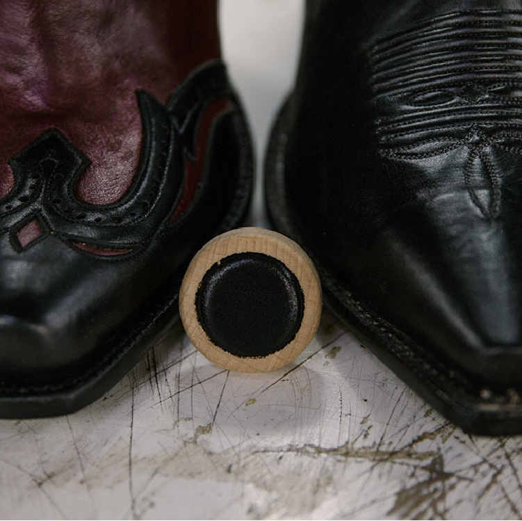 Black cowboy boot and black leather bottle cap.